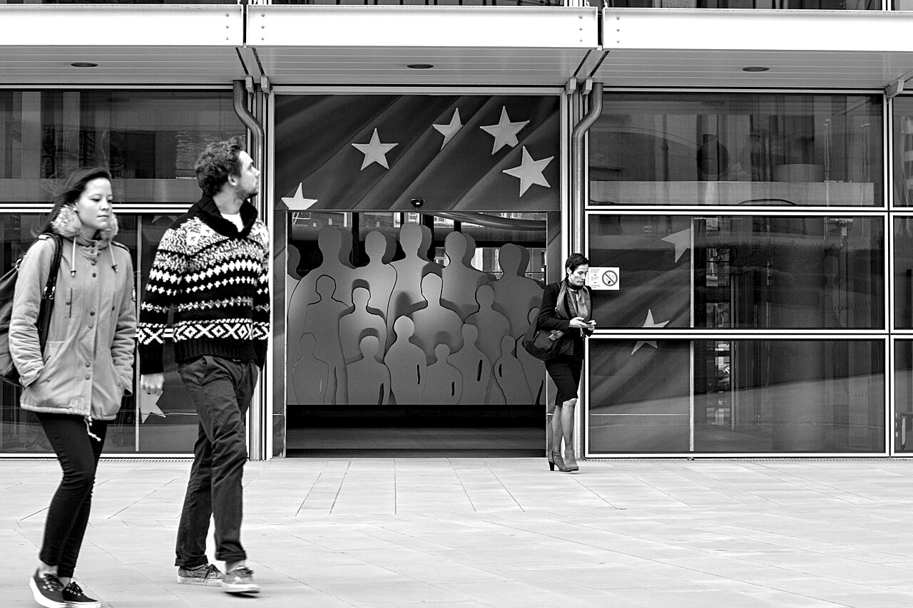 Fotografía de archivo · Fachada de edificio moderno con vidriera que muestra siluetas de personas y bandera con estrellas